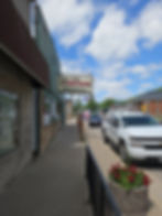 Street view of "The Stockyard Grill & Saloon." A white truck and other vehicles parked nearby. American flag visible, clear sky background.