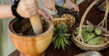 Fresh fruit and herbs being crushed with a wooden pestle to prepare elephant food