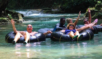 Cheerful travelers raising their arms while riding black inner tubes through a Khao Sok river