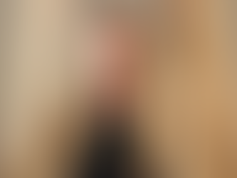 Smiling woman with long wavy blonde hair wearing a black top and brown cardigan. Neutral background, warm lighting, calm mood.