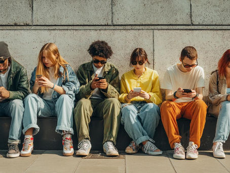 Six people sit on a concrete bench, engrossed in their phones, wearing casual outfits. The urban background adds a relaxed vibe.