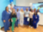 Group of people smile in a room with blue walls, balloons, and a "Congrats" banner. One holds a certificate. Celebratory mood.