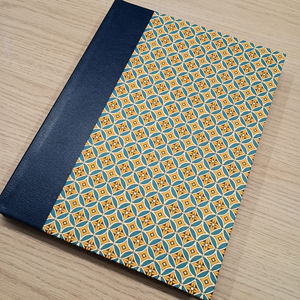 The completed hardback cover featuring a navy quarter binding and patterned Italian paper in teal, yellow, and white geometric motifs.