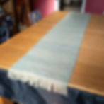 Extra-long handwoven table runner in soft sage and cream tones, styled along a wooden dining table.