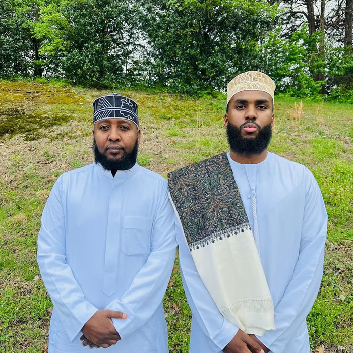 Two men in white robes pose outdoors; Dar Al-Quran Wa-Sunnah Institute.