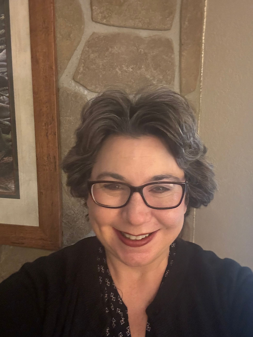 Sherri Hanks with glasses in front of a stone wall, wearing a black top and looking at the camera indoors.