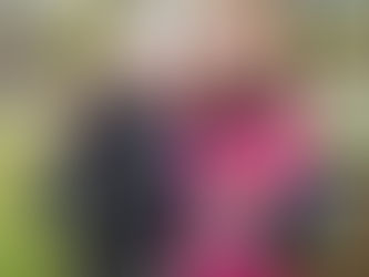 Two runners smiling, embracing post-race. One wears a medal and holds a water bottle. Both have bibs reading "New River Trail Races." Outdoor setting.