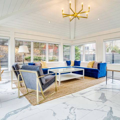 Sunroom with a white marble floor, blue sectional sofa, gold chandelier, and windows on nearly every side