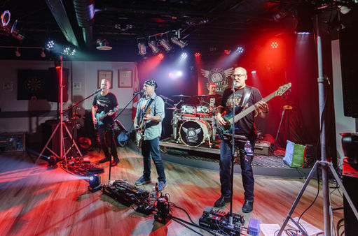 Rock band performing under red and blue stage lights, with two guitarists, a drummer, and a bassist in the foreground