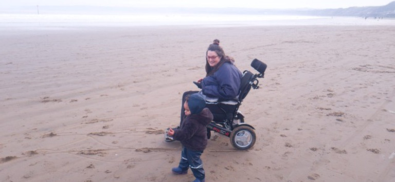 Smiling woman in wheelchair with child on beach