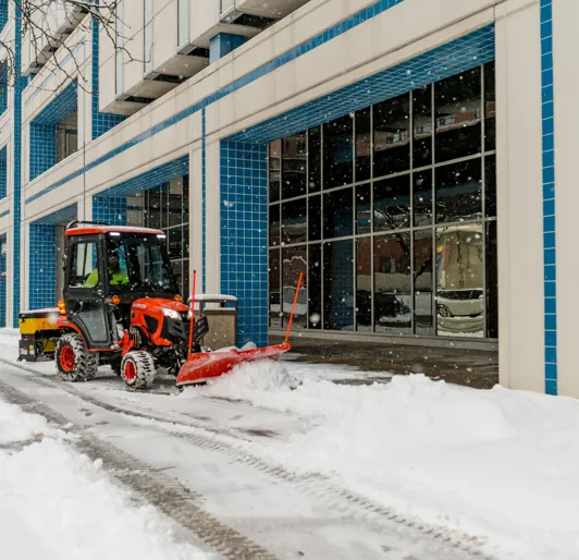 Small tractor clearing snow on commercial sidewalk