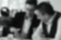 Jamie wears a dark suit and white shirt. Wearing dark rimmed glasses he demonstrates an up close card trick for a guest.