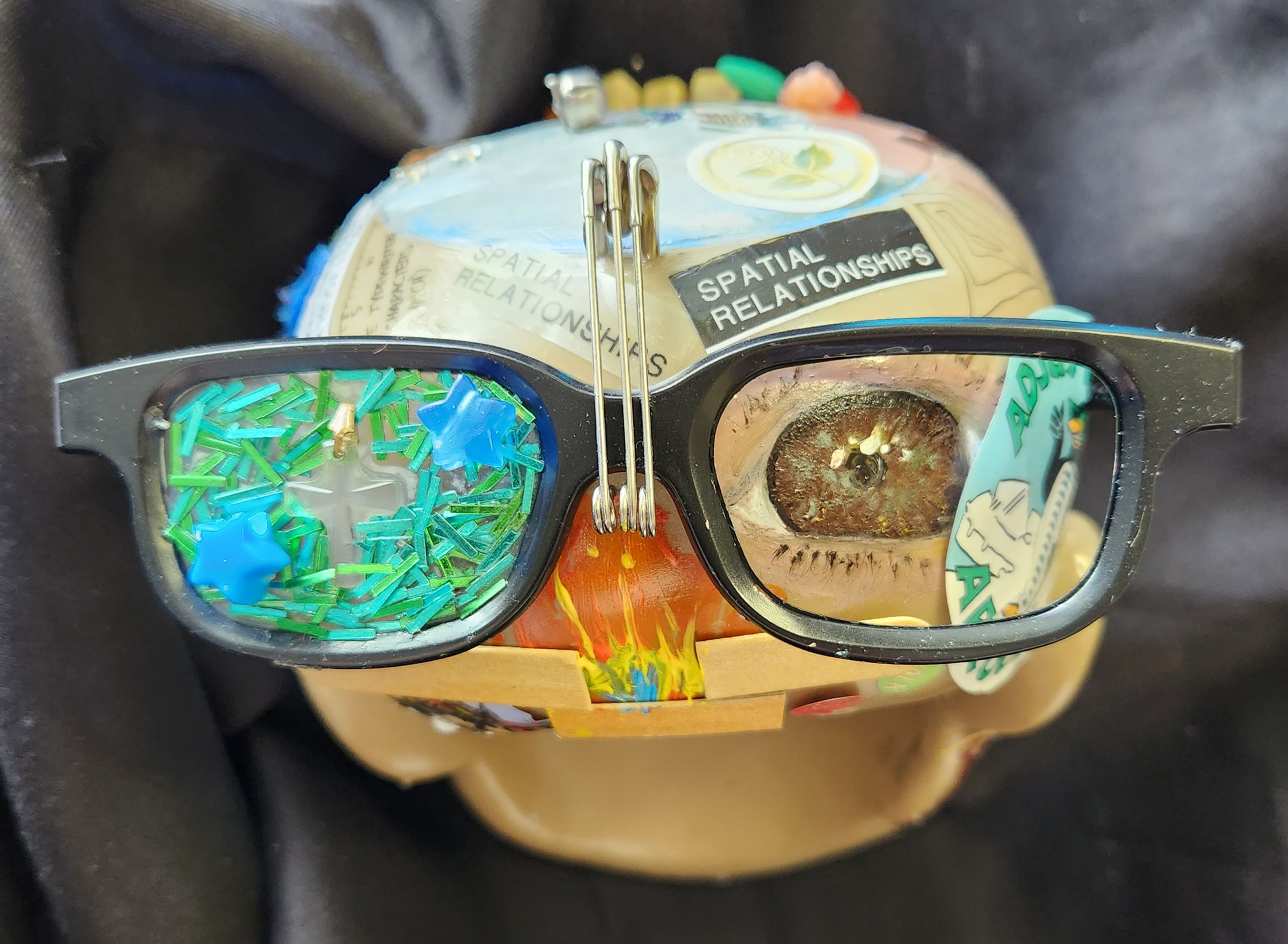 3D assemblage art of a mannequin head with sunglasses and pins