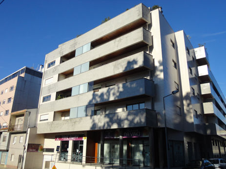 Perspetiva de esquina do Edifício Santa Tecla, fachada moderna em cinza claro, varandas largas e lojas no piso térreo.
