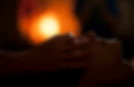 a dark room with warm lighting behind the face of a person with light skin whose face is being touched by the hands of a second person with light skin