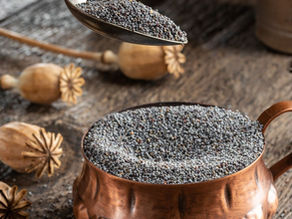 Makové zrnká v medenej nádobe a lyžici na drevenom stole