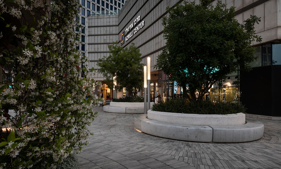 כיכר עירונית מחוץ למרכז עזריאלי עם ריצוף אבן, עצים נטועים באדניות בטון ותאורת רחוב מודרנית