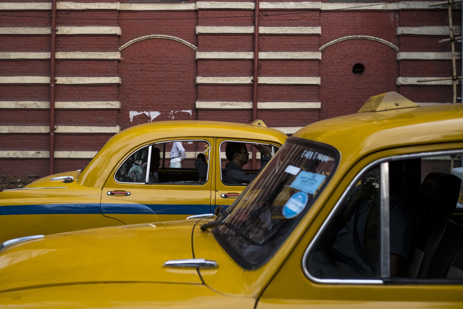 Des taxis Ambassador jaunes près d'un bâtiment en briques rouges à Kolkata.