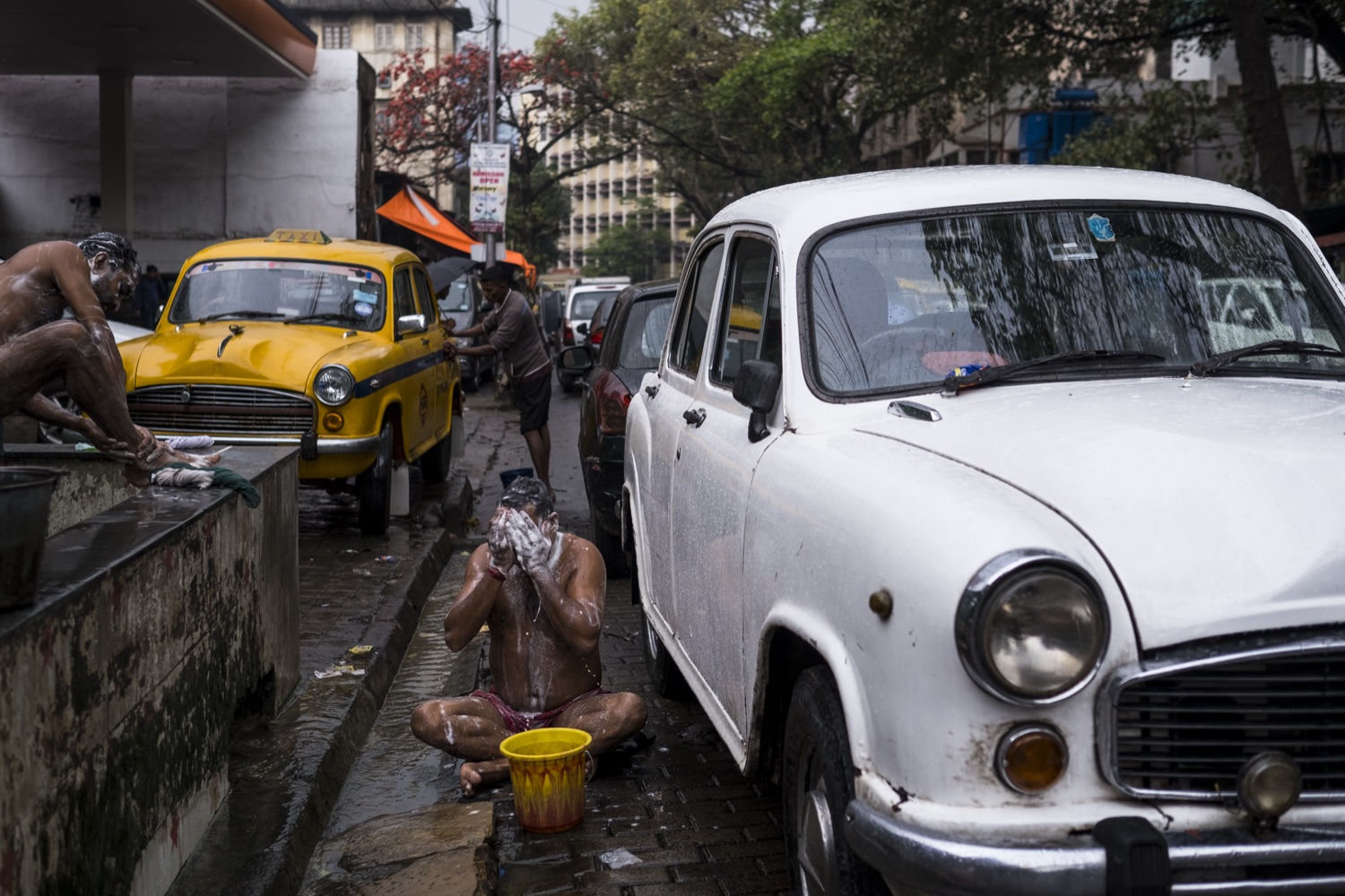Un homme se lave près d'un point d'eau dans la rue, à côté d'une Ambassador blanche et d'un taxi jaune à Kolkata.