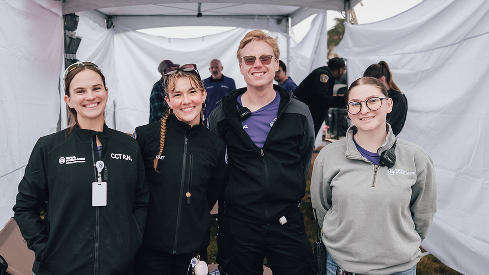 Four smiling Royal Ambulance staff in black and gray jackets pose under a white tent, with CCT R.N. and EMT text visible.