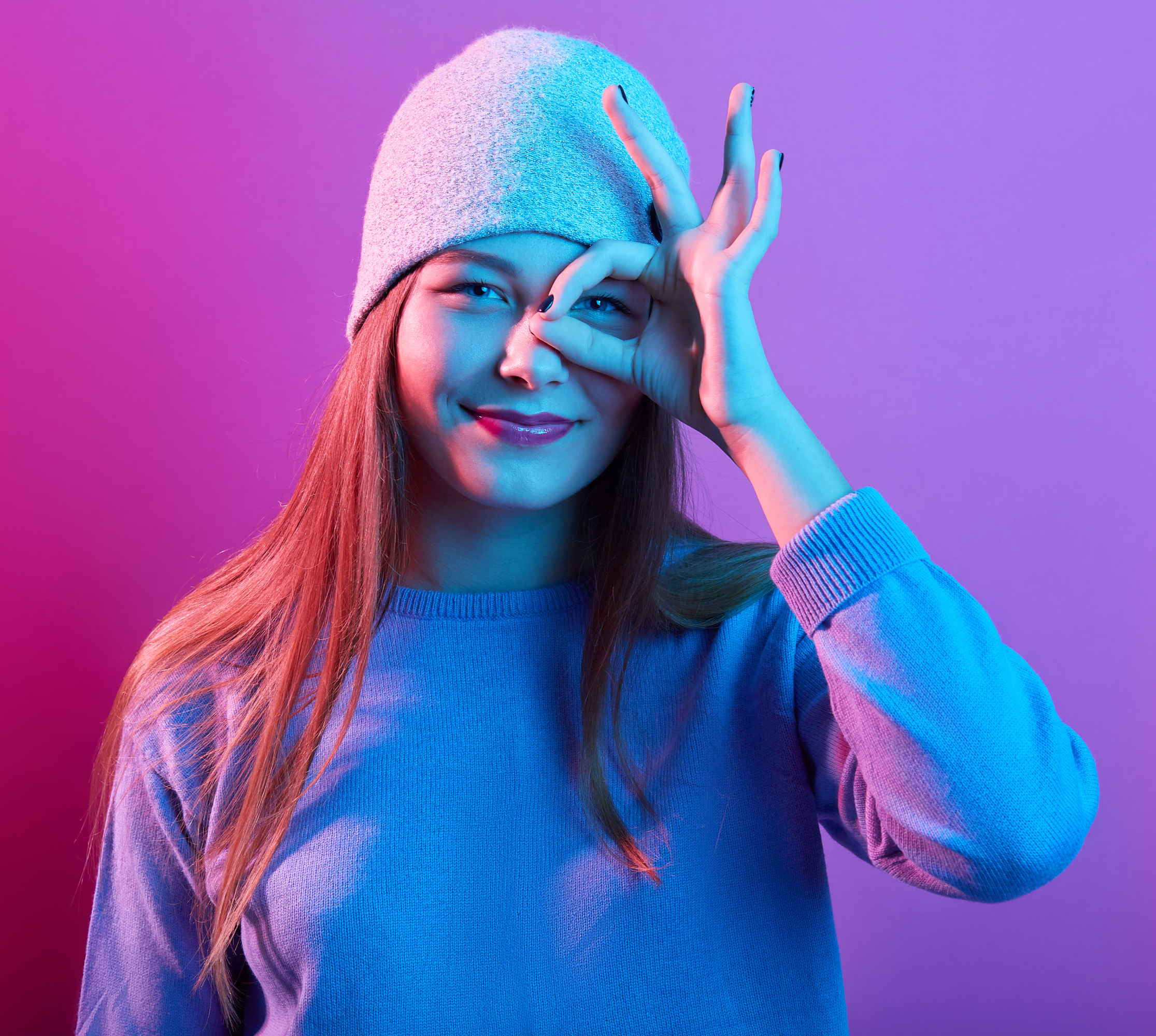 portrait-excited-young-woman-dressed-casual-sweater-knitted-hat-showing-ok-sign-against-he
