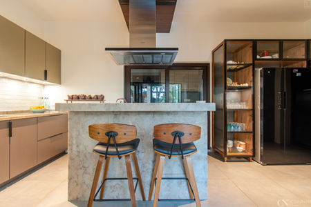 This kitchen in Bangalore features a modern style, with an island , bar stools and glass crockery unit with black frames.