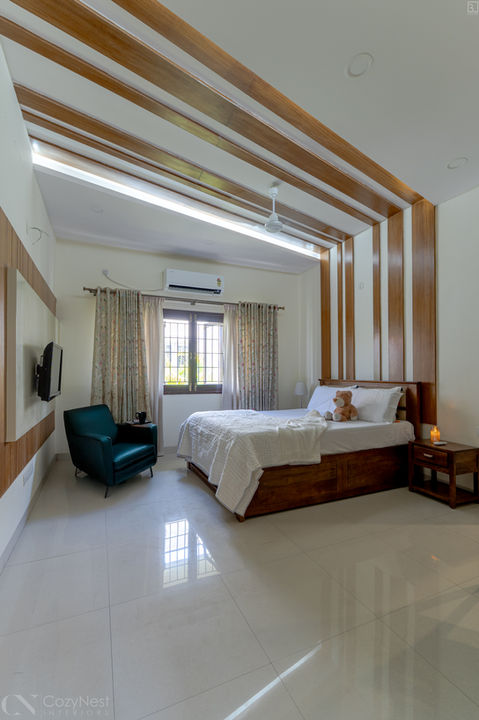 Modern spacious bedroom with a white tile floor, a wooden bed frame with white bedding, an aqua velvet armchair, and dramatic vertical and horizontal wood slatted paneling extending from the wall onto the ceiling.