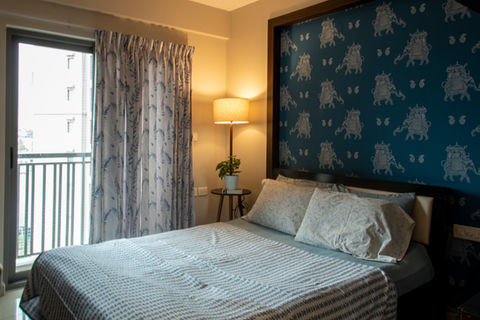 Contemporary bedroom design featuring a dark bed against a vibrant blue and white patterned wallpaper accent wall, with natural light coming from the balcony door.