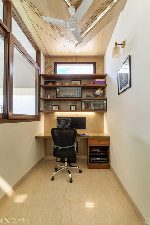 Compact and modern home office featuring pale wood veneer walls and ceiling with geometric score lines, built-in floating wooden shelves, a desk with an ergonomic black chair, and a small horizontal window above the monitor.