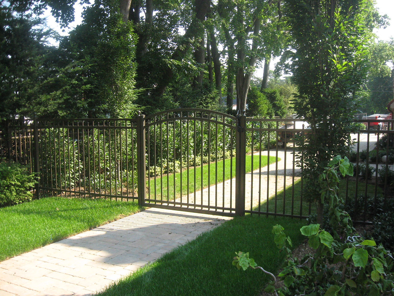 Black metal fence with gate, greenery, and walkway. North Shore Fence Co.