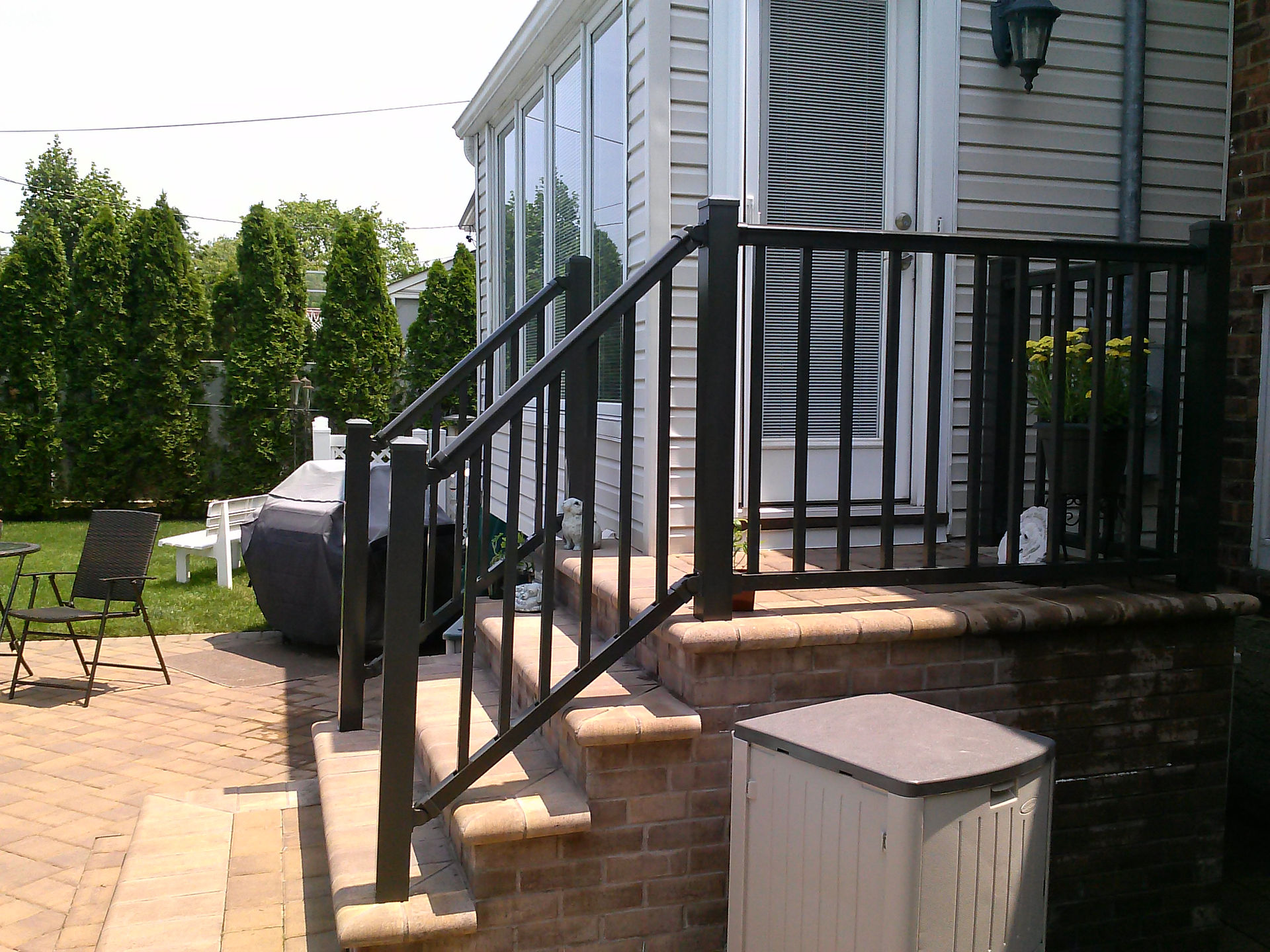 Black railing on deck with stairs and trees in background.