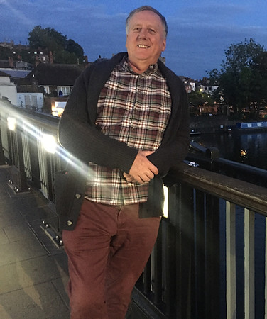 Man smiling on bridge at dusk, canal boats visible