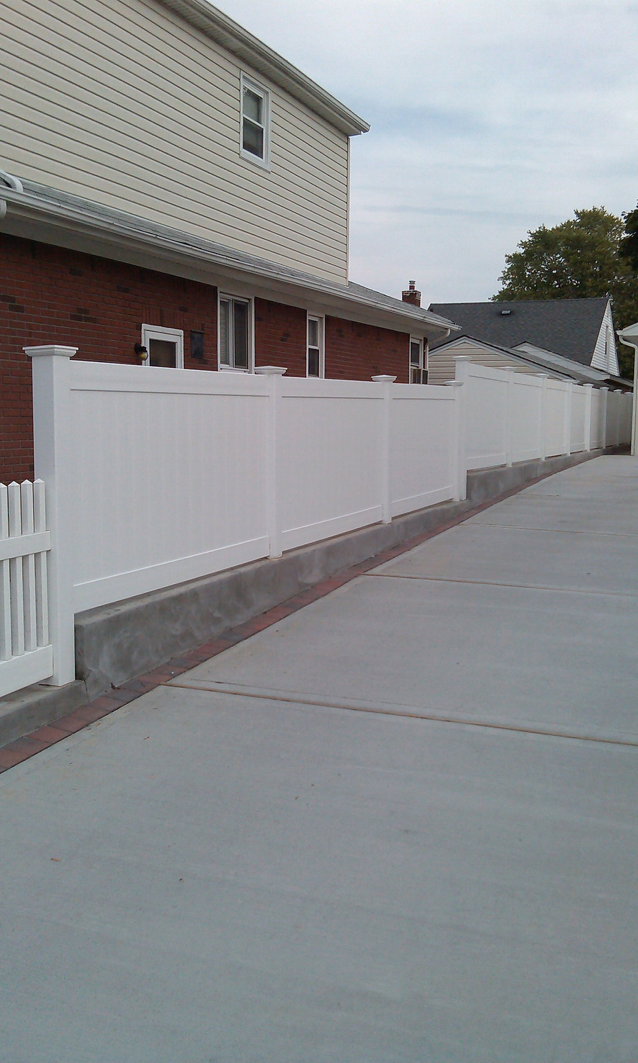 White vinyl fence along driveway, house in background. North Shore Fence Co. 