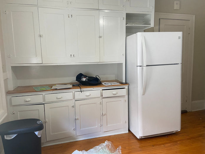 Outdated kitchen with white cabinets, mismatched hardware, and cluttered countertop.