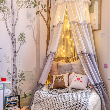 Canopy reading nook with twinkle lights, gray knit blanket, and animal pillows in a woodland-themed children’s playroom.
