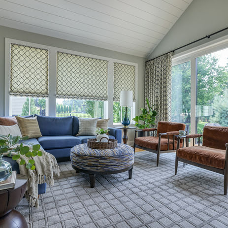 Sunroom with blue sectional sofa, patterned roman shades, and woven ottoman coffee table