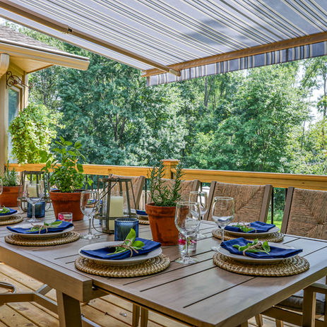 Outdoor dining table on deck with place settings, plants, and striped awning