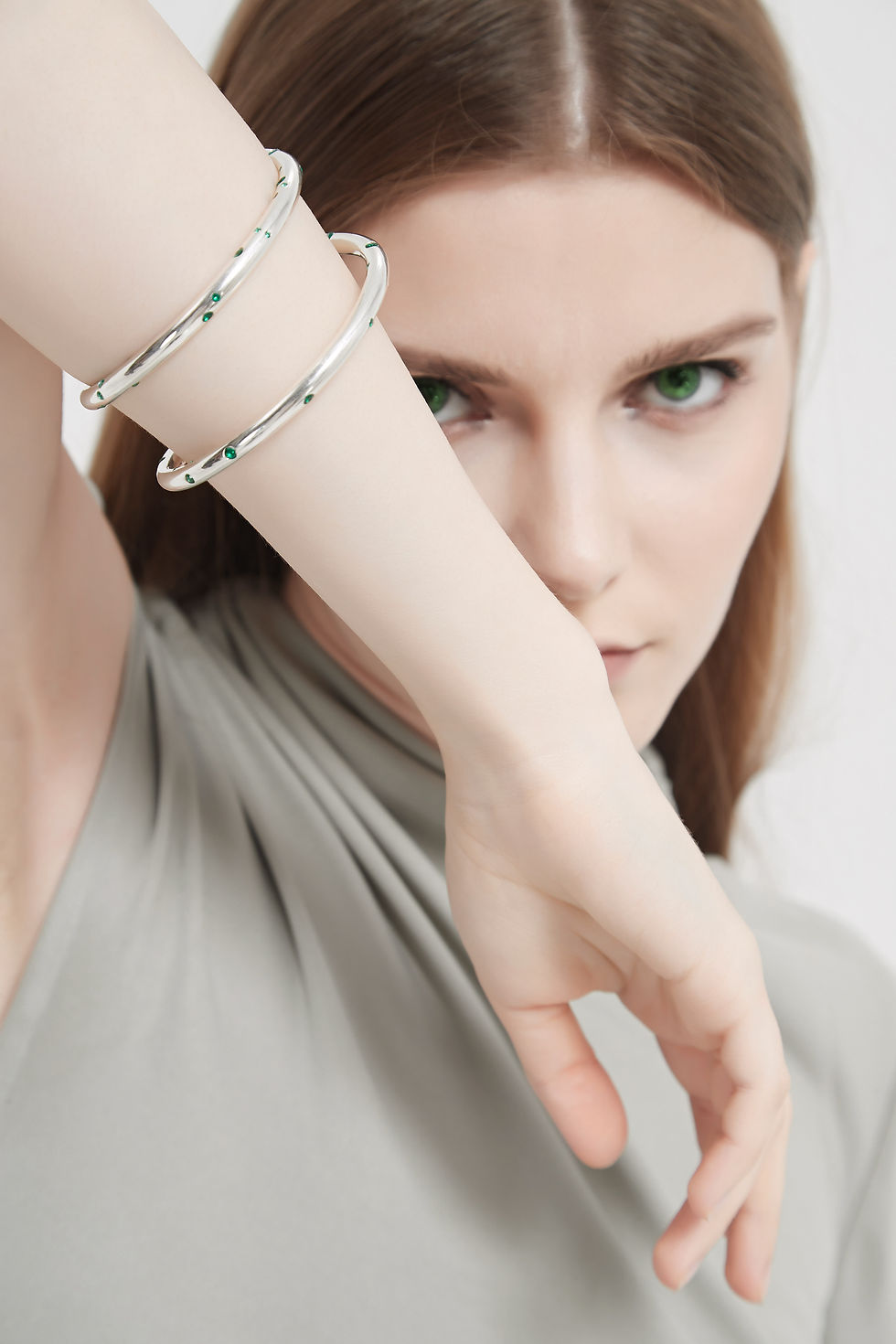 Woman posing with a spiral shape silver made hand cuff setted with green diamonds