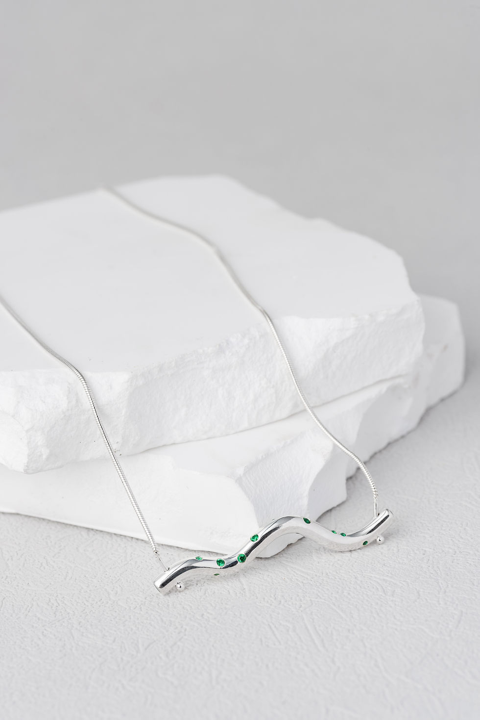 Wavy shape silver made necklace charm setted with various sizes of green diamonds