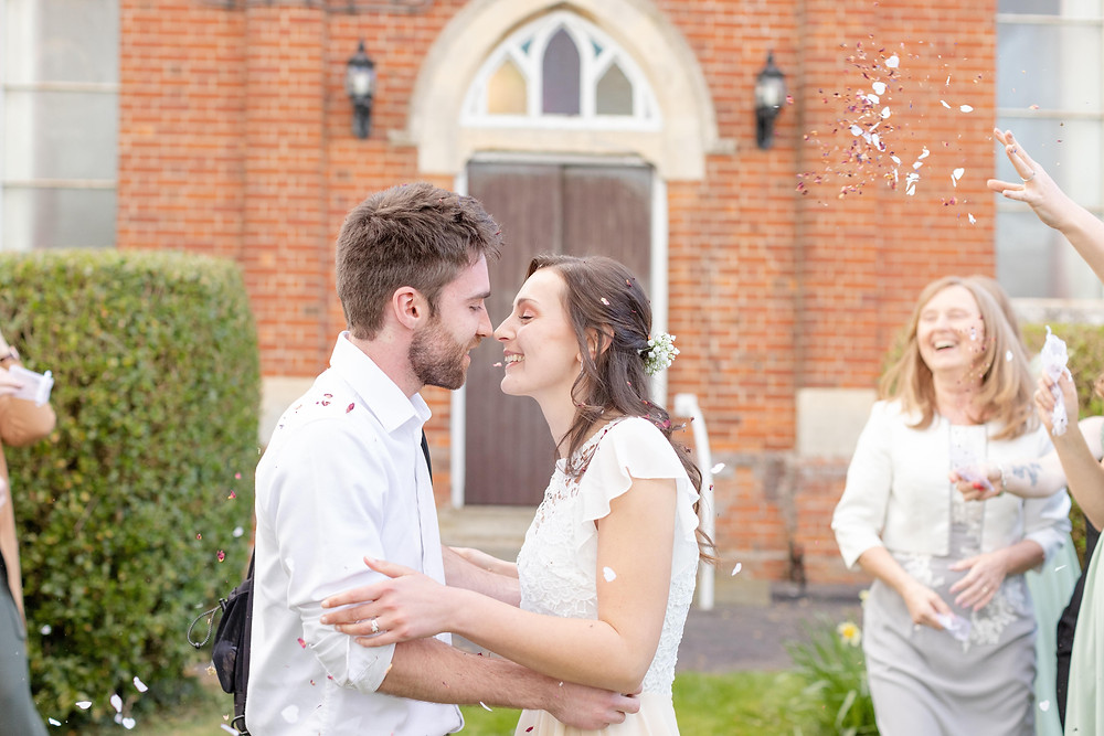 Bride and groom go in for a kiss as their guests shower them in biodegradable confetti