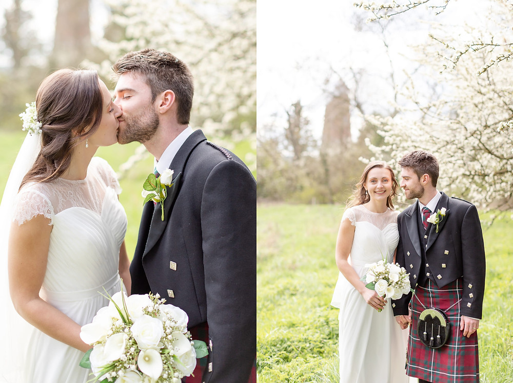 bride and groom kiss under white blossom trees. bride smiles and groom looks at bride, a windmill in Quainton is visible in the background