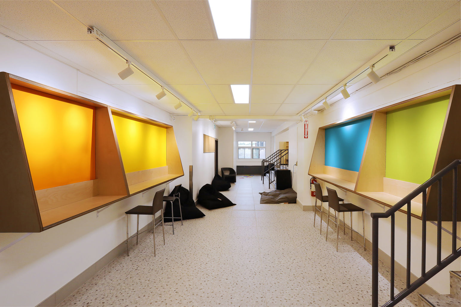 Corridor d'une école primaire dont les murs sont longés par 4 bureaux de travail flottants et colorés. Projet de rénovation avec rafraîchissement des locaux, classes, École La Fourmilière, dans la Capitale-Nationale