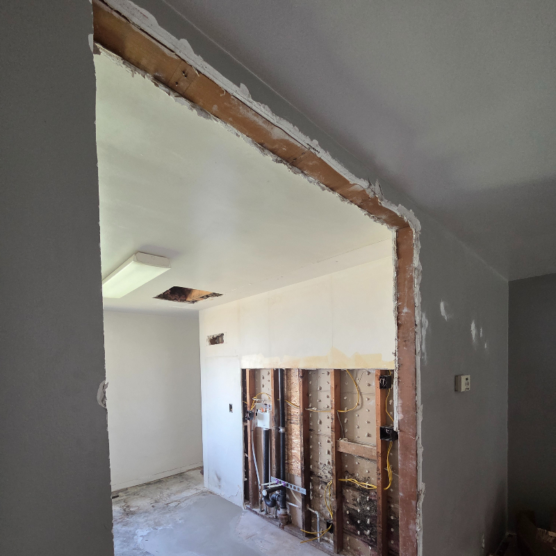 Large wall opening exposing wood lath and framing after kitchen utility upgrades in an older Utah Valley home.