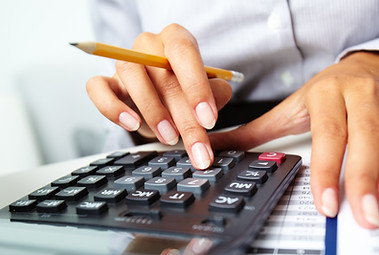 Photo of hands holding pencil and pressing calculator buttons over documents