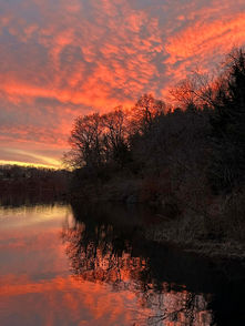 Dramatic sunset over lake with fiery clouds and tree reflections in water