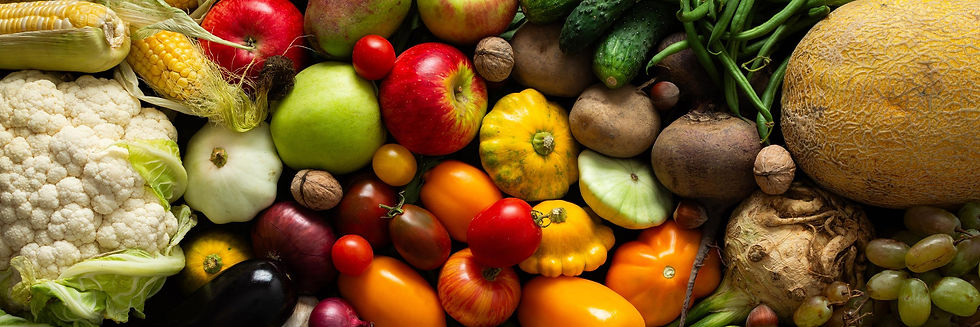 A vibrant assortment of fresh fruit and vegetables tightly arranged together, including red and green apples, cherry tomatoes, heirloom tomatoes, red onion, pumpkin, corn with husk, walnuts, and dark eggplant, creating a colourful and textured produce display.