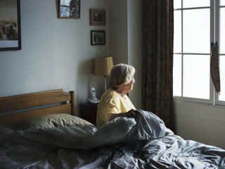 Elderly woman looking out of window in bed