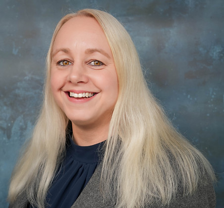 Headshot of Louise, female with long blonde hair wearing a grey blazer and dark blue top looking to the page centre.