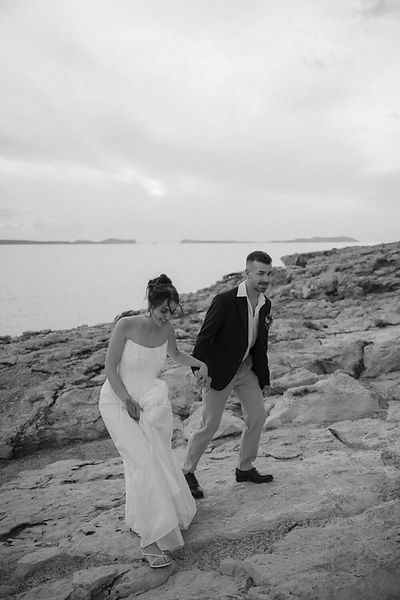 bride and groom walking across rocks at seaside wedding