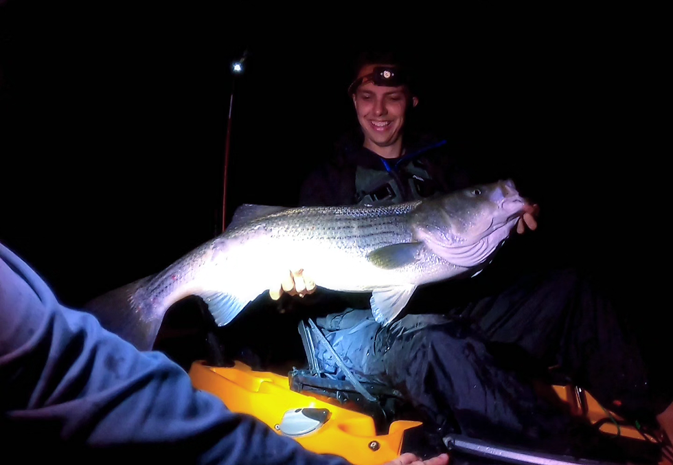 Thumbnail: A happy client with a solid striped bass caught at night in a kayak with CT Fish Nerd